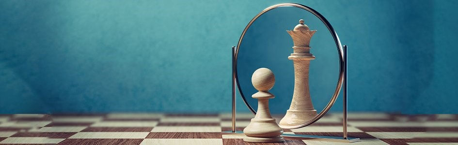 A pawn chess piece looking into a circular make-up mirror and seeing a queen chess piece.