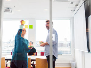 Colleagues putting sticky notes on a glass wall