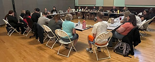 A group of people working around a grouping of tables.
