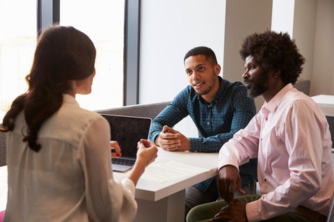 A woman at a desk talking to a Black student and his father
