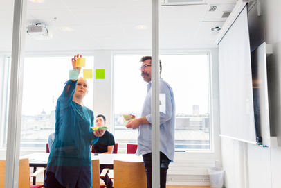 Colleagues putting sticky notes on a glass wall