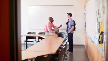 A teacher talking to a student in an empty classroom