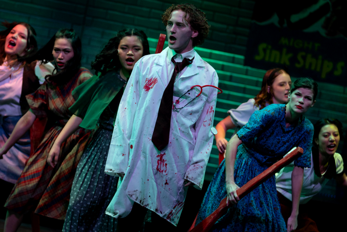 Bloody doctors stands eerily in front of a dirty crowd of dancers holding red firearms.