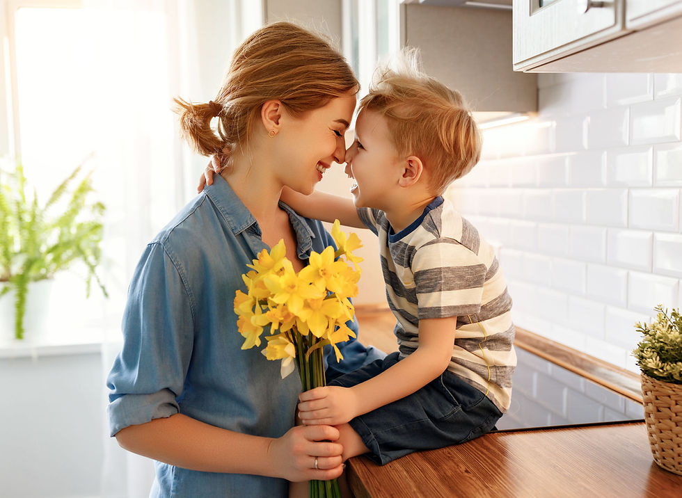 A cheerful boy smiling and hugging his mother with a bouquet of flowers