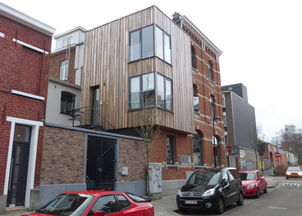 Hoekgebouw met een moderne houten uitbouw en grote ramen bovenop een traditionele bakstenen gevel, gelegen in een stadsstraat met geparkeerde auto’s.