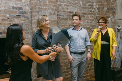 A group of business owners, one speaking in a microphone, other receiving flowers