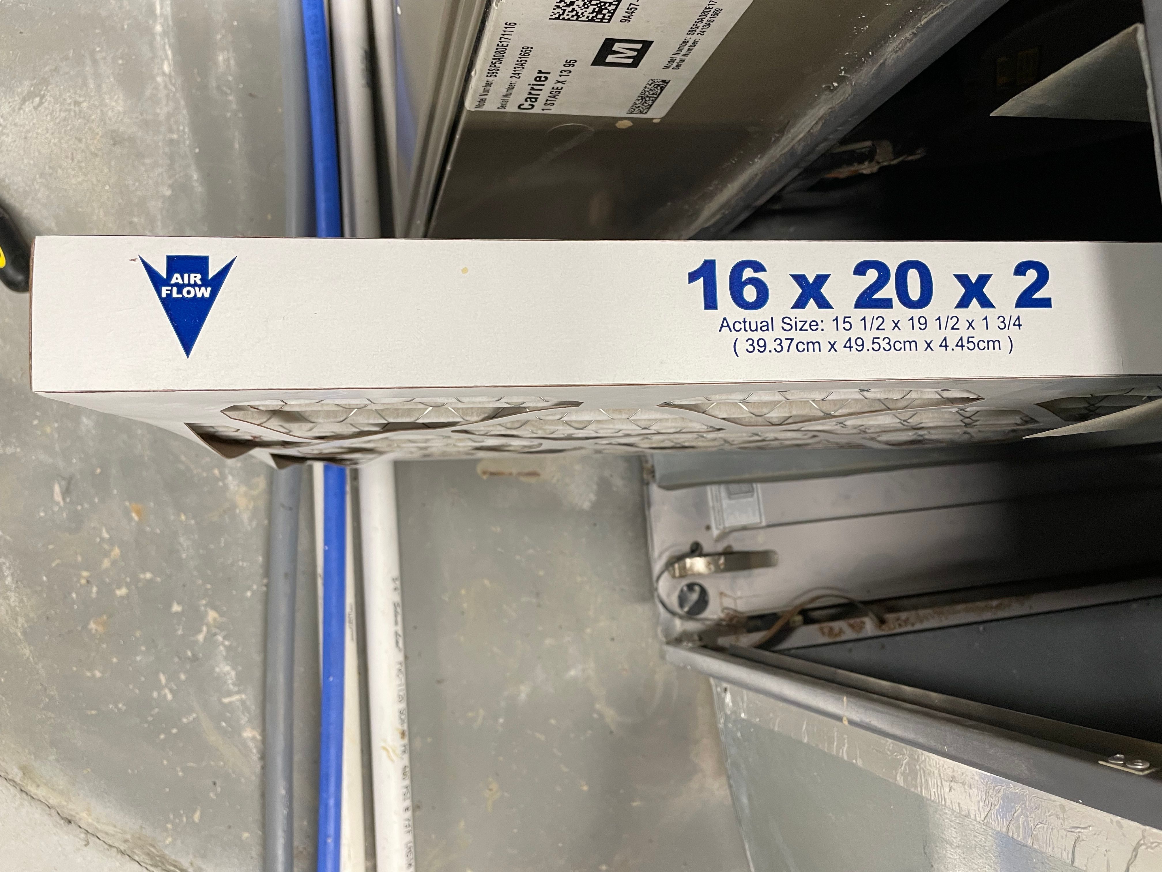 Photo of an HVAC filter that's been pulled partly out of the HVAC unit. We see a side view showing an arrow for which way the arrow flows (and which way to put it in) as well as the sizing information of 16 x 20 x 2 for this particular filter. 
