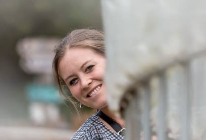 "Rebecca Saavedra, founder of Seniorly Haven, smiles while peeking playfully from behind a structure.jpeg