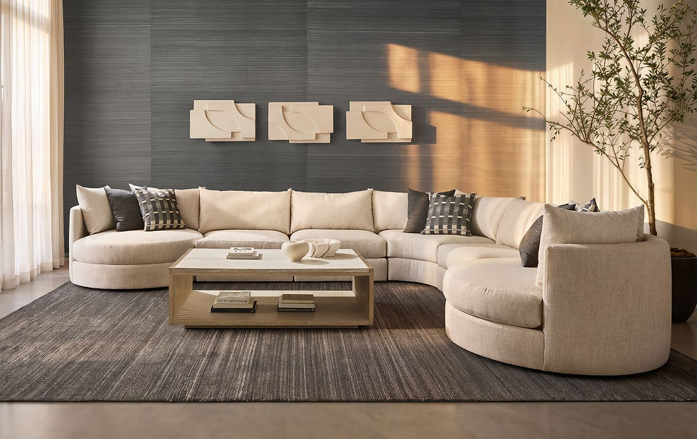 Sunlit modern living room with beige sectional, coffee table, art wall, potted tree, and books; calm, airy mood.