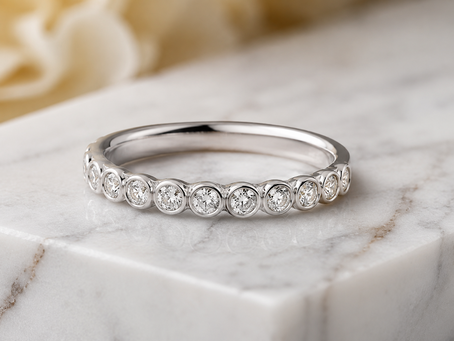 White gold diamond eternity ring on a white marble block, with a soft warm blurred background.