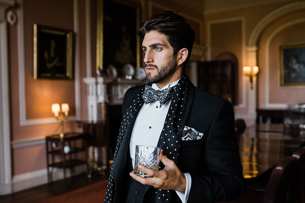 Eye-level view of a groom adjusting a patterned bow tie with a tailored navy suit