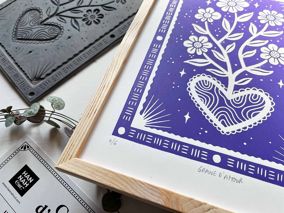 Miniature : Une main tient un cadre en bois contenant une linogravure intitulée Graine d’Amour, représentant un cœur fleuri