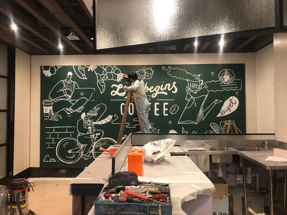 咖啡店內牆面彩繪工程施工現場,展示工匠搭設木質A字梯對黑板牆面頂部進行線條彩繪細節施作