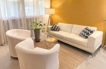 Heller Praxisraum mit Sofa, Sessel und warmem Licht – ein ruhiger Ort zum Ankommen vor dem Termin