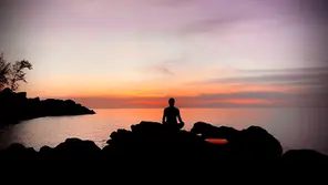 Silhouette einer meditierenden Person auf einem Felsen am Meer bei Sonnenuntergang – Sinnbild für die Kraft der Stille und die Suche nach innerer Ruhe.
