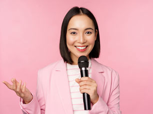 femme-d-affaires-asiatique-prononcant-un-discours-tenant-un-microphone-et-souriant-debout-en-costume-sur-fond-rose