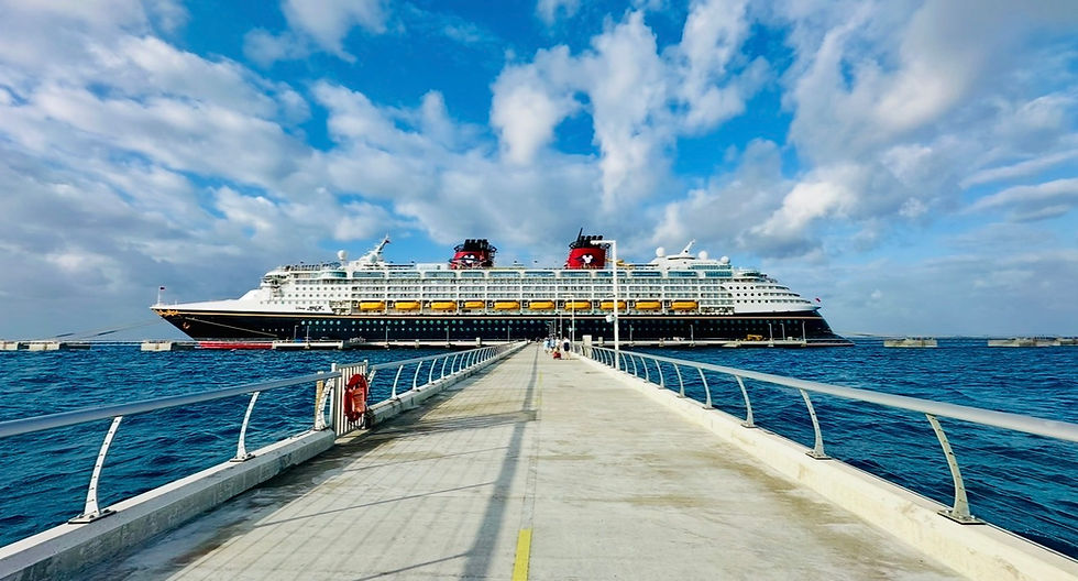 Disney Cruise ship docked at the end of a long pier, surrounded by turquoise water beneath a partly cloud sky.
