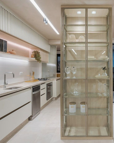 Uma cozinha com móveis planejados, móveis planejados na cor branca, com eletrodomésticos embutidos, e uma estante planejada com vidros.