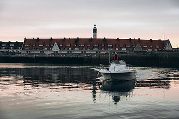Bateau de pêche amarré au port de Calais au coucher du soleil, phare en arrière-plan