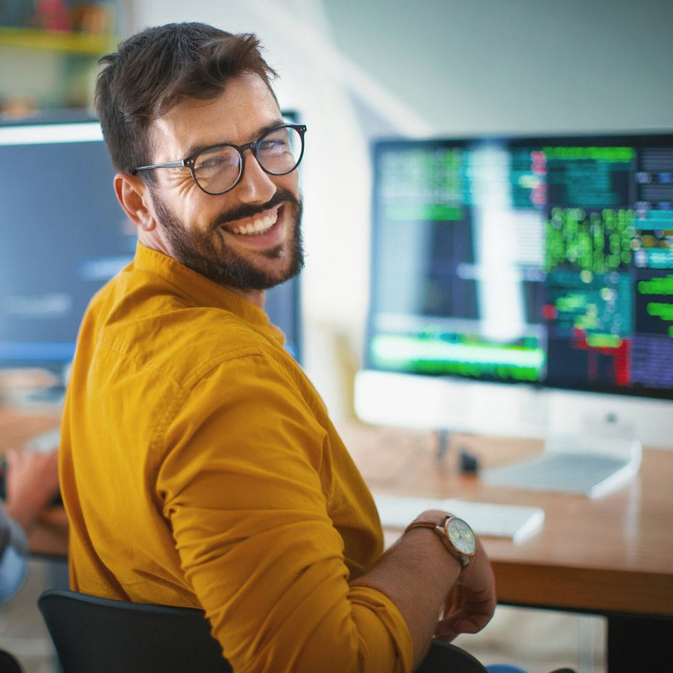man wearing yellow shirt and glasses sits at a desk with computer