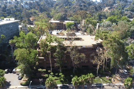 An aerial view of a modern commercial office building complex in Mission Valley, San Diego, surrounded by green trees and parking lots.