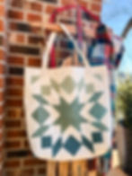 A cream and green quilted tote hanging on a wood sled in front of a red brick wall.