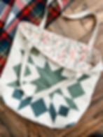 Cream and green star quilted tote with a floral lining on a wood floor.