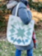 A woman in a winter coat and jeans holding a cream and green star quilted tote bag outside.