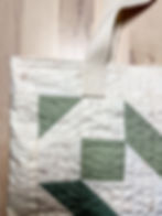 A cream and green tote bag with cream handles and two seams sewn around the top edge.