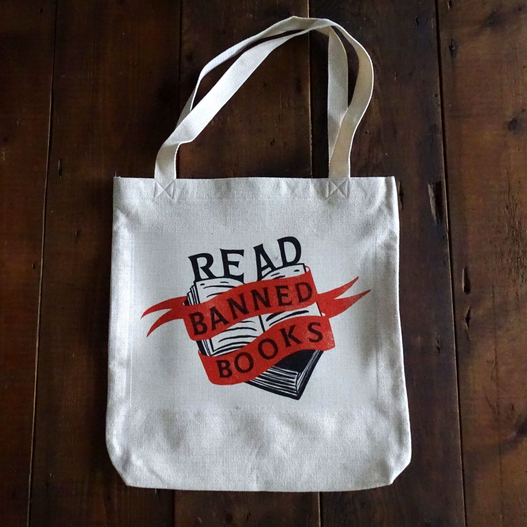 White tote bag with the slogan Read Banned Books is laying on a wooden background