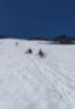 a mountain top in snow with three people sledding down (close up)