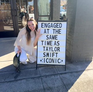 Tiff posing on front of a sign that says "engaged at the same time as taylor swift iconic
