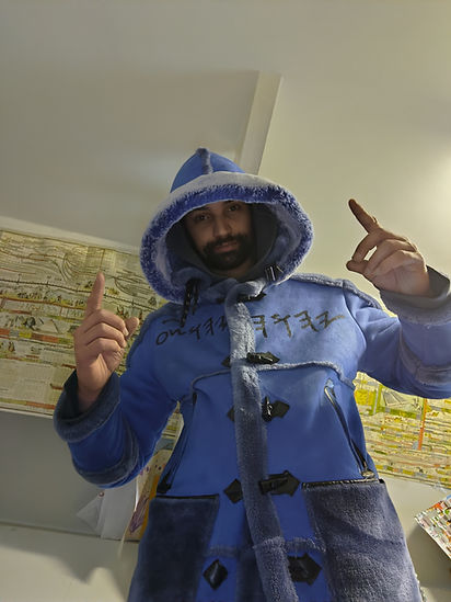 Man wearing blue hooded coat points up, facing the camera; indoors