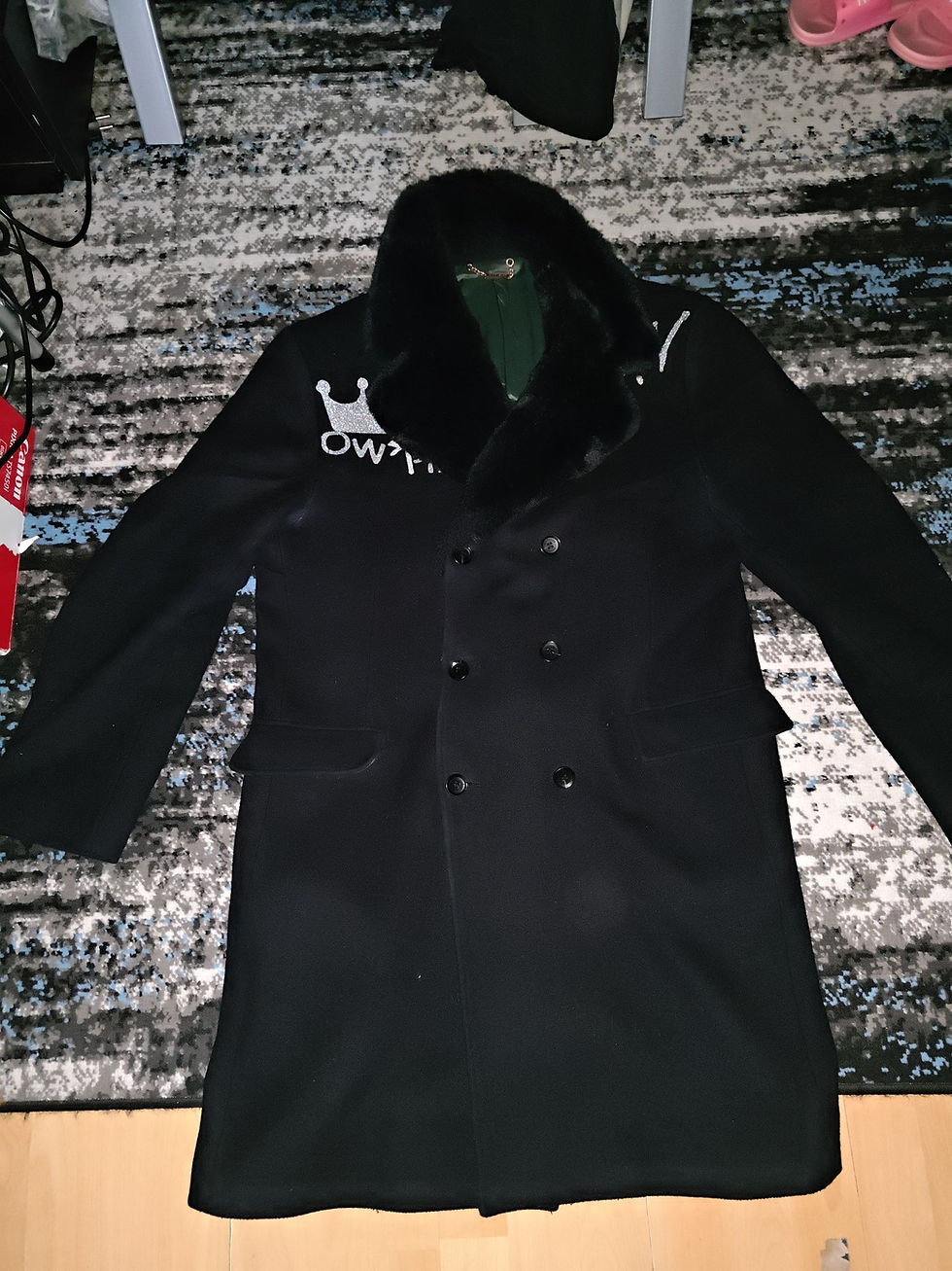 Black coat with OWTT text, cap blood of 𐤉𐤄𐤅𐤔𐤏 𐤉𐤄𐤅𐤄, on a patterned rug; Yahusto