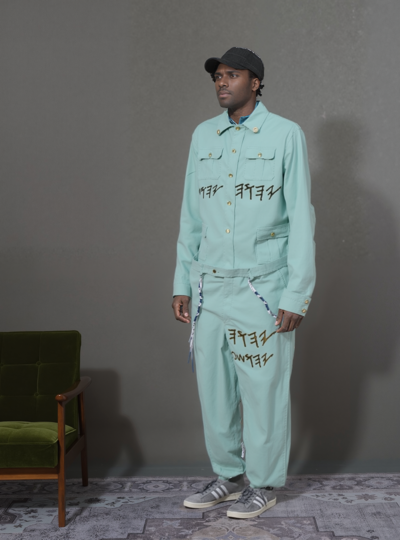 Man in mint jumpsuit with Hebrew text; YaHU YaHUsHa bead chain; standing by chair
