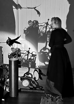 Interactive shadow theater where two practitioners navigate a room in total darkness, working on paper carvings using torches and lights.