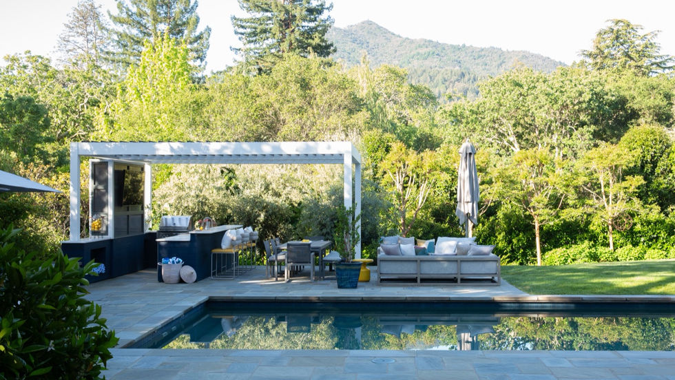 Poolside outdoor kitchen and lounge framed by mature trees and a wooded hillside.