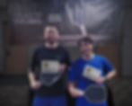 Two smiling men hold paddles and "Congrats!" signs in front of a "SALT Pickleball" banner. Indoor setting, casual attire.