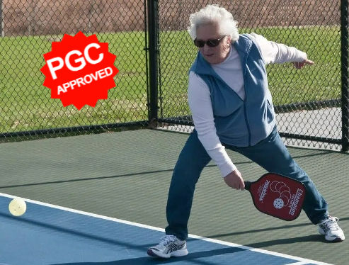 An older woman playing pickleball outside.