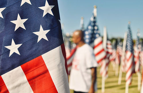 Close up picture of a US flag with a blurry background of a black man and more US flags._e