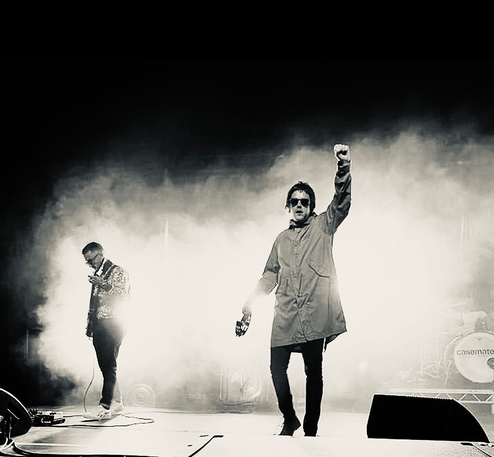 Two performers on stage, one raises a fist and the other holds a guitar. Bright backlight with mist. 