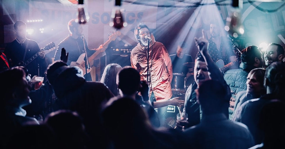 Band performing on stage with a singer in a red jacket, surrounded by an excited crowd in a dimly lit venue. Blue and purple lighting.
