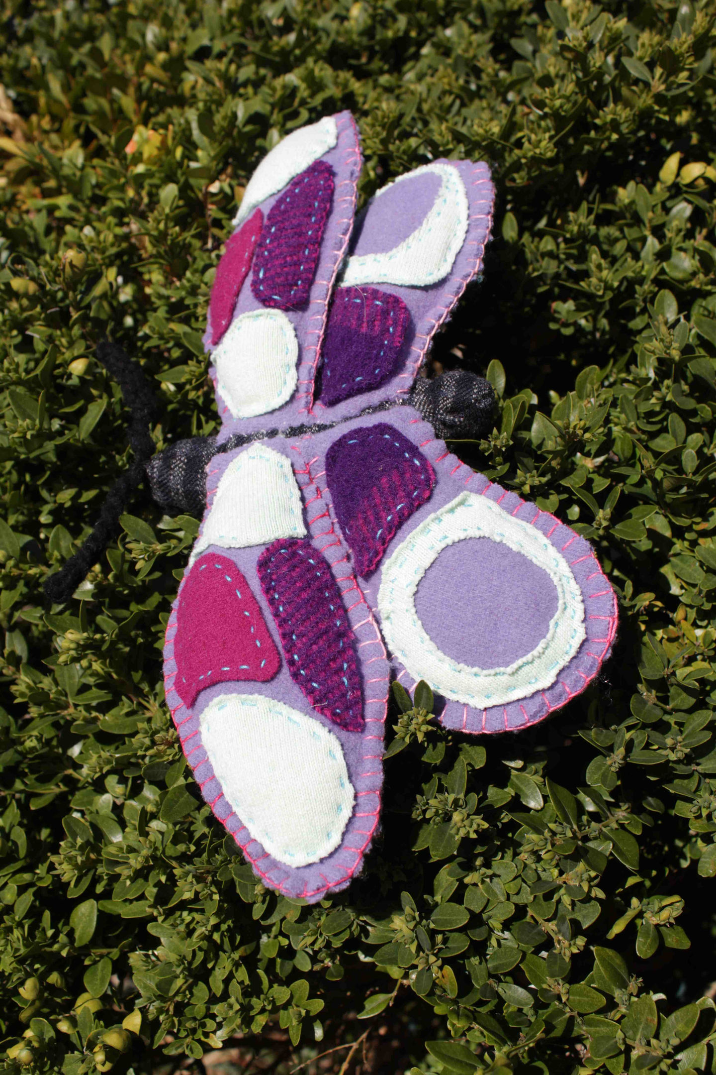 a purple and pink stuffed butterfly is sitting on a bush