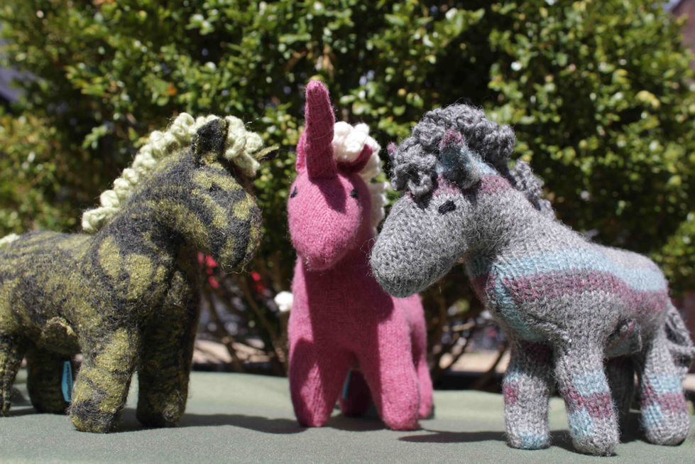 three stuffed animals are sitting on a table including a pink unicorn