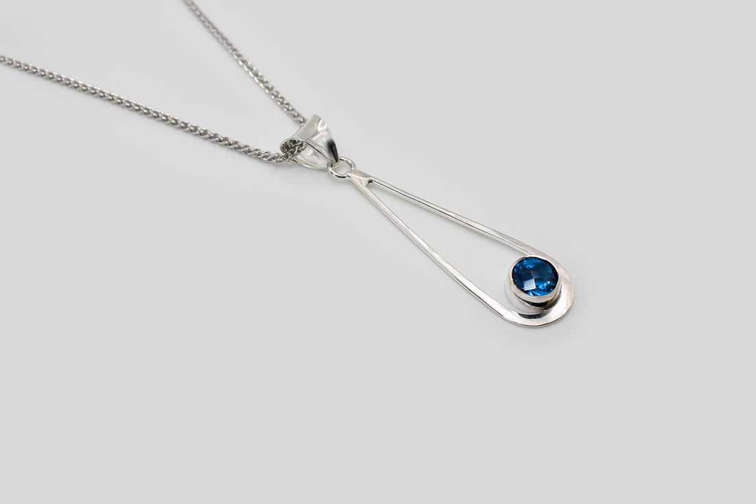 Silver necklace with sapphire blue pendant on white background