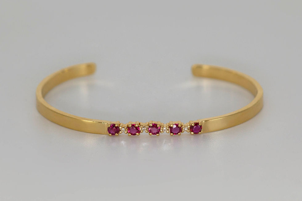 Gold open cuff bracelet with five magenta gemstones on a white background, shown in a simple product-style view