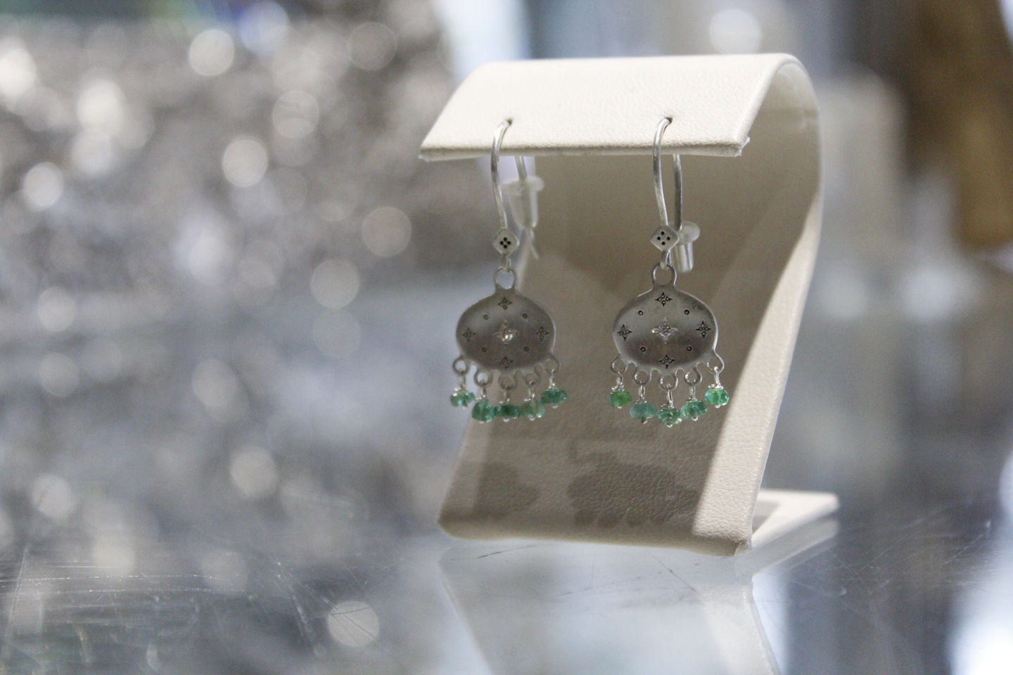 a pair of silver earrings with green beads hanging from them