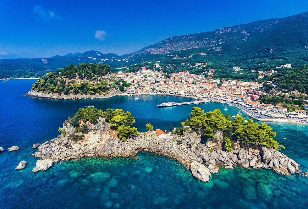 A stunning aerial view captures the picturesque coastal town nestled between lush green hills and the sparkling azure waters. A rocky peninsula dotted with vibrant vegetation extends into the sea, framing a serene bay where a few boats are anchored.