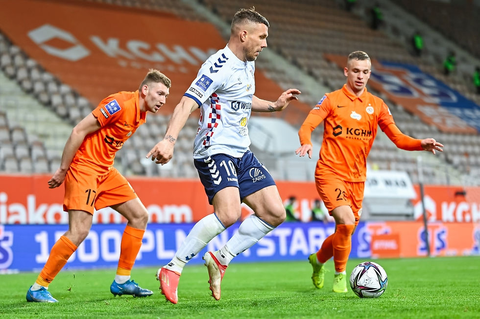 A player in a white and blue uniform skillfully controls the ball while evading two opponents in orange kits during an intense football match.