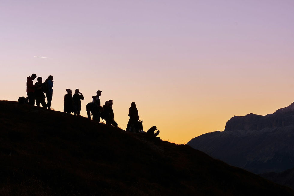 A group of hikers gathers on a hilltop, silhouetted against a stunning, golden sunset with mountains in the distance, capturing the serene beauty of nature.